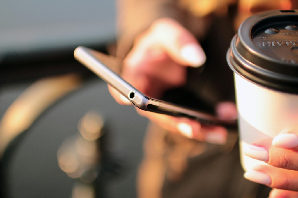 Hands holding a smartphone and a coffee cup in warm outdoor light